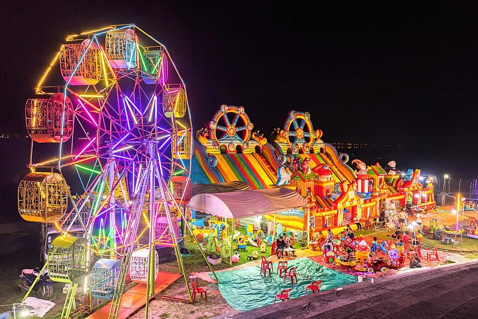 Illuminated Ferris wheel, bouncing castle and carousel at night in a funfair in Vientiane, Laos